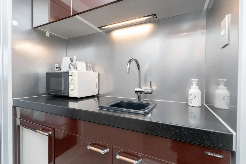 ミニキッチンには電子レンジ、湯沸かしポット、小さなシンク付き。あたたかいごはんを室内で。