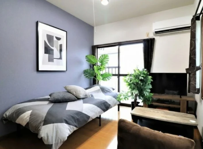 ブルーのデザインクロスがおしゃれな１Kのお部屋！　座椅子付きでテレビを見ながら自宅のようにお過ごしいただけます。※植木と額は写真用です。