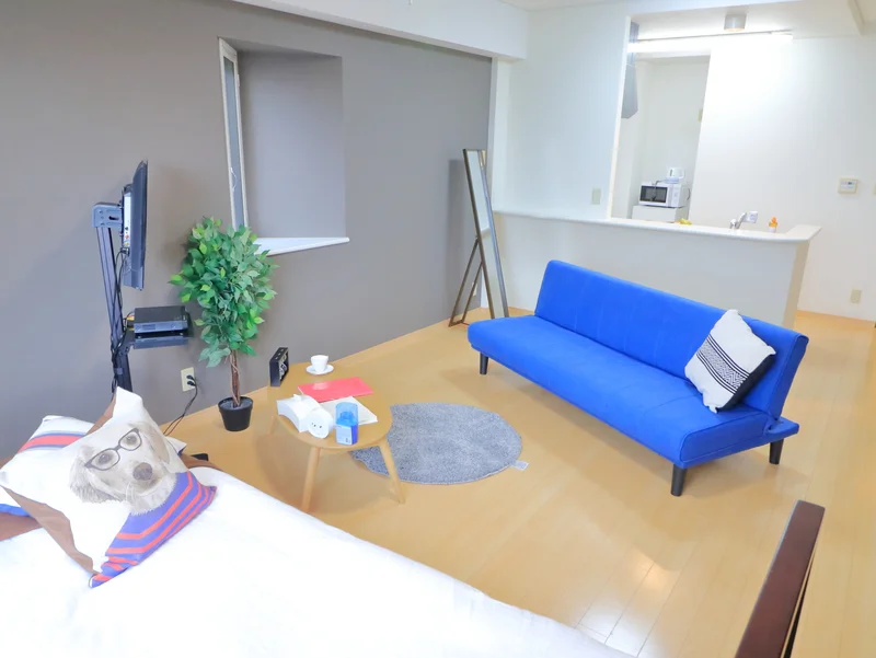 ソファ付きの広めの洋室です　明るい色味のインテリアが魅力的！　デザインクロスがおしゃれな対面キッチンがあるマンスリーマンション！